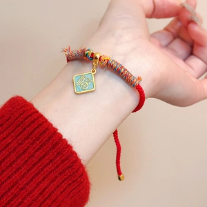 Détail d'un bracelet tressé rouge avec pendentif doré portant le caractère Fu