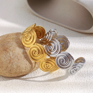 Close-up of geometric spiral bangles in gold and silver finish on a natural stone
