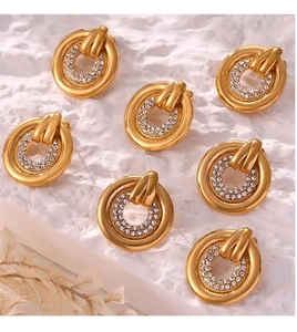 Flat lay of gold circular earrings with pavé white zircon stones on a white textured surface