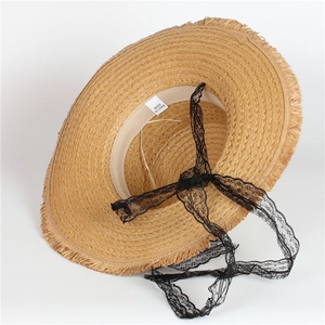 Detail of flat top straw hat featuring frayed edges and elegant black lace tie ribbons