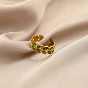 Detailed close-up of adjustable gold ring with green enamel leaves on silk fabric