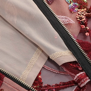 Detail of red floral embroidery with colorful sequins and metal zipper on mesh fabric