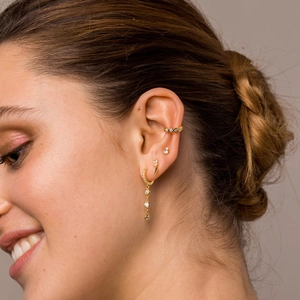 Close-up of gold chain earrings and zircon ear cuffs worn on a model's ear