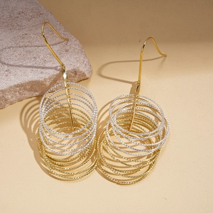 Detail of mixed-metal layered hoop earrings with beaded texture on a stone base