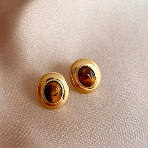 Close-up of vintage gold stud earrings featuring polished tiger's eye stones on soft satin.