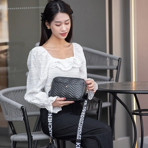 Detail of black quilted V-pattern camera bag with stylish logo-print woven strap