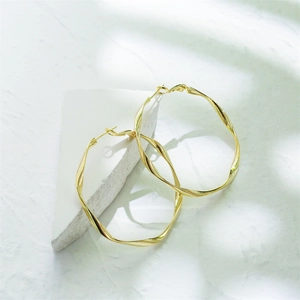 Polished 14K gold plated geometric twist hoop earrings on a minimalist white stone background