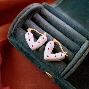 Boucles d'oreilles cœur à pois blancs et rouges avec bordure dorée sur velours