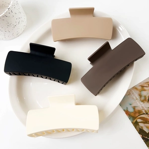 Set of four matte solid square hair claws in beige, black, and brown on a white tray