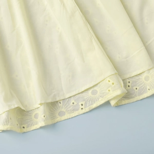 Detail of yellow cotton dress hem featuring intricate floral embroidery and eyelet lace