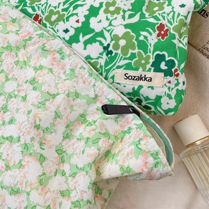 Macro detail of green floral makeup pouches with durable zippers on linen background
