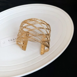 Detailed view of a gold-layered hollow woven cuff bracelet on a white ceramic plate