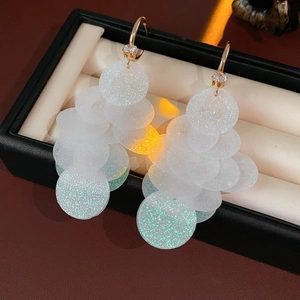 Detail of sparkling sequin tassel C-shape earrings with gold hooks on a display case