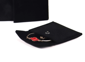 Detail of a black velvet jewelry pouch with snap button holding a gold enamel bracelet