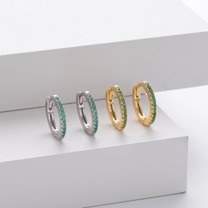 Detail of silver and gold huggie earrings with micro-set green cubic zirconia stones