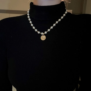 Nahaufnahme Perlenkette mit Goldmünzen-Porträtanhänger auf schwarzem Rollkragen