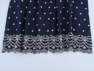 Detailansicht des dunkelblauen Hemdkleides mit weißen Stickereien und gewelltem Saum