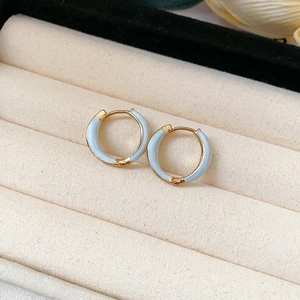 Detail of light blue enamel hoop earrings in gold plating on a beige velvet jewelry box