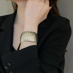 Detail of wide gold cuff bracelet featuring vertical textured stripes on model wrist
