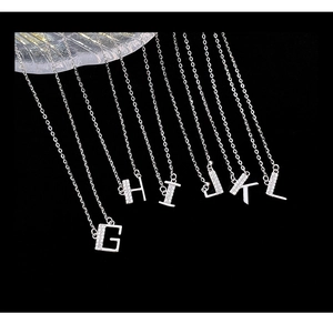 Macro detail of silver S925 alphabet pendants G to L with pavé diamonds on black background
