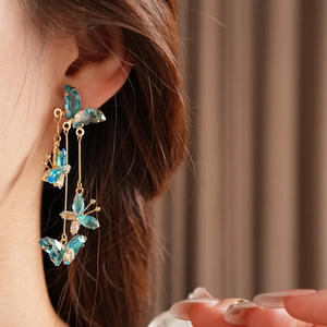 Vue détaillée de boucles d'oreilles pompons dorées avec breloques papillons bleu translucide