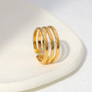 Detailed view of a gold triple-layer hollow open ring on a textured white surface