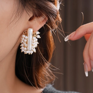Gros plan de boucles d'oreilles dorées avec perles blanches sur un mannequin en gris