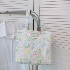 Detail of floral quilted tote bag with a simple wish label on soft fabric surface