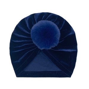 Detailed view of dark blue velvet baby turban hat with soft plush pompom decoration
