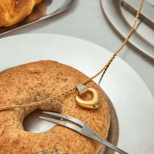 Collier cœur doré avec strass présenté sur un décor créatif avec un bagel et une fourchette