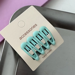 Macro view of four matte mint green teardrop hair clips on beige display card