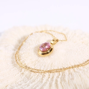 Detail of gold necklace featuring an oval pink gemstone pendant on a refined chain
