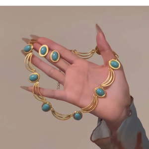 Detail view of a vintage gold-toned jewelry set with green turquoise stones held by hand