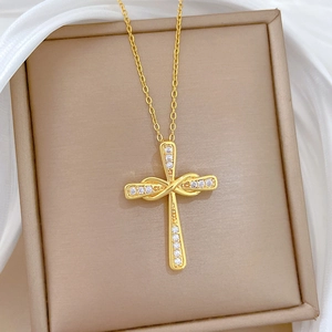 Dettaglio del ciondolo a croce ritorta dorata con cristalli su portagioie beige elegante