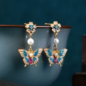 Detail of enamel butterfly earrings with pink gemstones and white pearls on gold frame