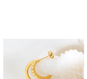 Detail view of twisted and polished gold hoop earrings resting on white coral