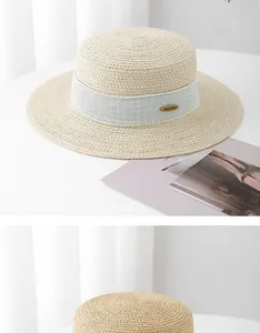 Detailed macro view of beige flat top straw hat featuring a blue ribbon and logo plaque