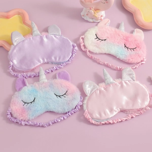 Flat lay of colorful plush and silk unicorn sleep masks with cute embroidery on pink background