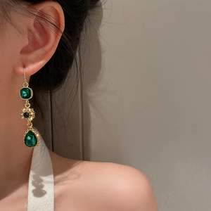 Macro detail of long vintage emerald green drop earrings with gold floral settings