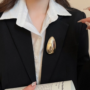 Detail of a minimalist gold teardrop brooch with high-polish finish on a black blazer