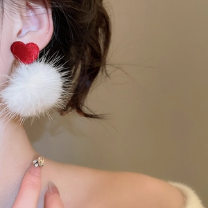 Détail des boucles d'oreilles cœur rouge avec pompons blancs sur l'oreille du mannequin