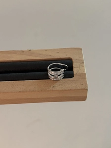 Close-up of silver ear cuff with H-shaped zircon inlay on a wooden stand