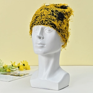Detail of yellow and black knit beanie featuring long fluffy fringe textures on a mannequin