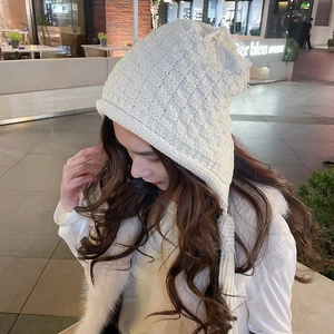 Detail of cream chunky knit pointed beanie with braided tassels on urban street background