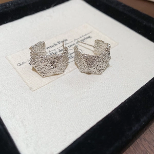 Macro shot of silver C-shaped earrings featuring a unique hammered lava texture finish