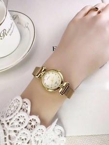 Close-up of golden vintage quartz watch with mesh strap and elegant bone china cup
