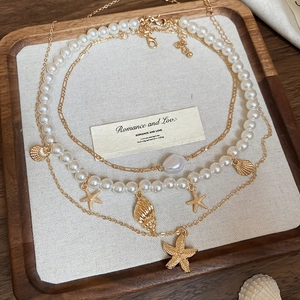 Detail view of multi-layered necklace with gold starfish, seashell charms and white pearls
