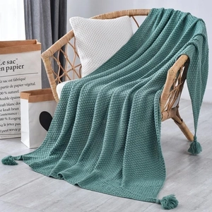 Detail of green knitted blanket with tassel edges on a rattan chair in soft light
