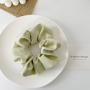 Detail of light green satin scrunchie showing smooth silky texture on a white decorative tray