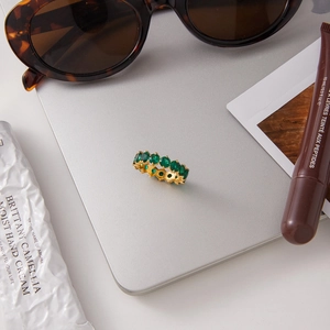 Detailed close-up of a gold ring with green zircon stones on a fashion accessory layout